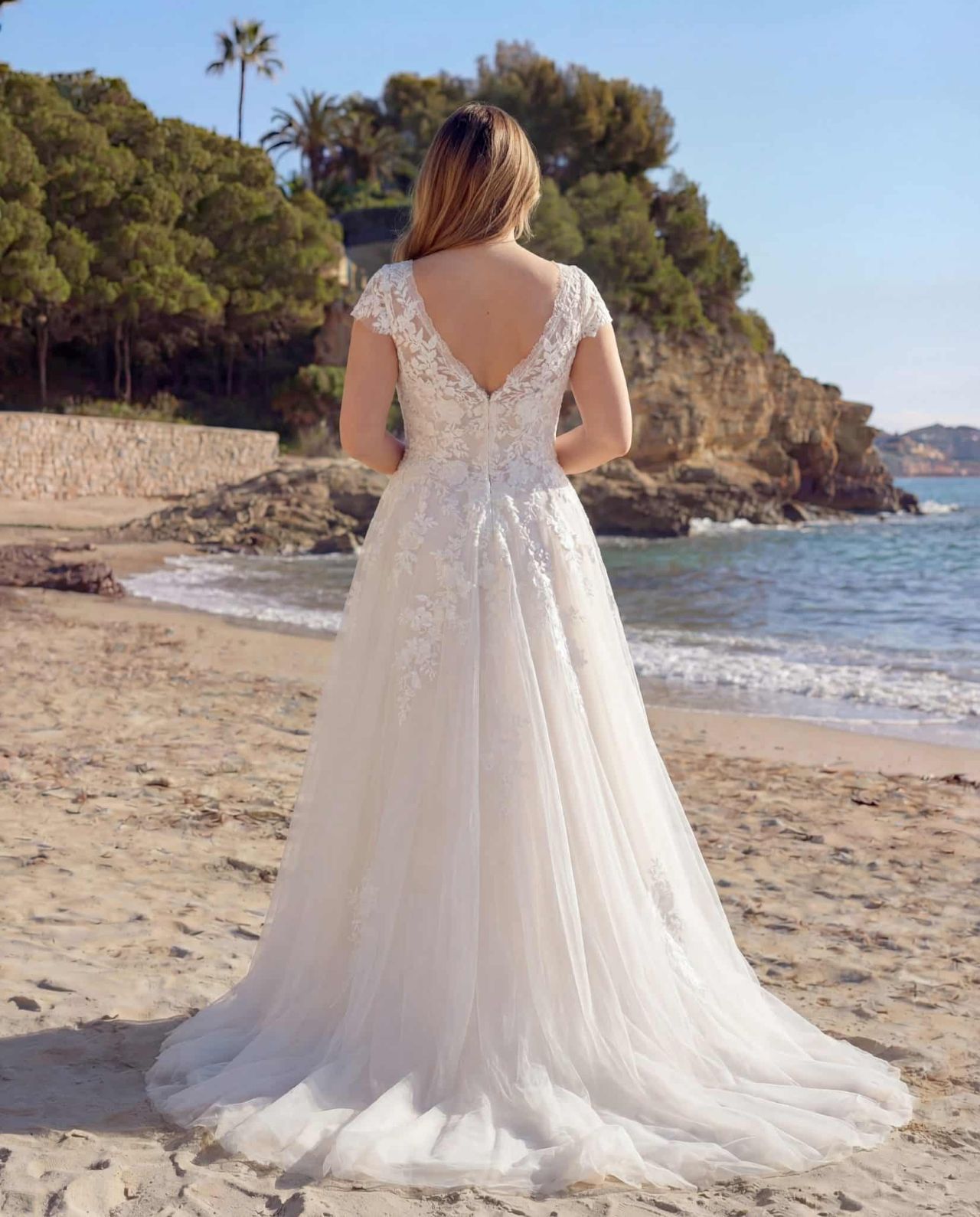 Romantisches Curvy-Hochzeitskleid mit V-Ausschnitt, kurzen Spitzenärmeln, floralen Applikationen, fliessendem Tüllrock und zarter A-Linien-Silhouette – Brautmode bei Brautfashion in Sins