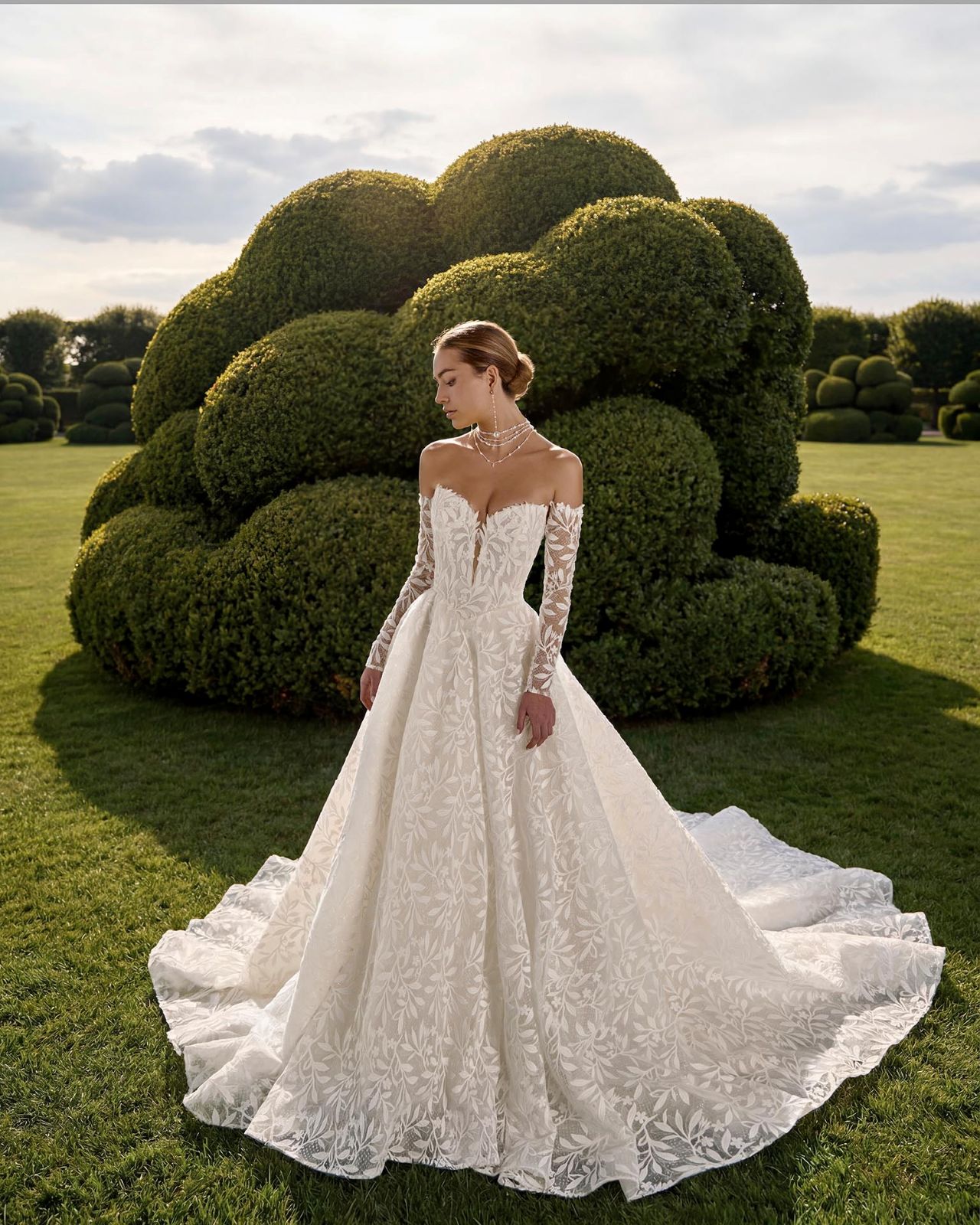 Romantisches Hochzeitskleid mit Off-Shoulder-Spitzenärmeln, floraler All-over Lace, herzförmigem Ausschnitt, voluminöser A-Linie, tiefem Rücken und langer Schleppe – Vorder- und Rückenansicht bei Brautfashion in Sins