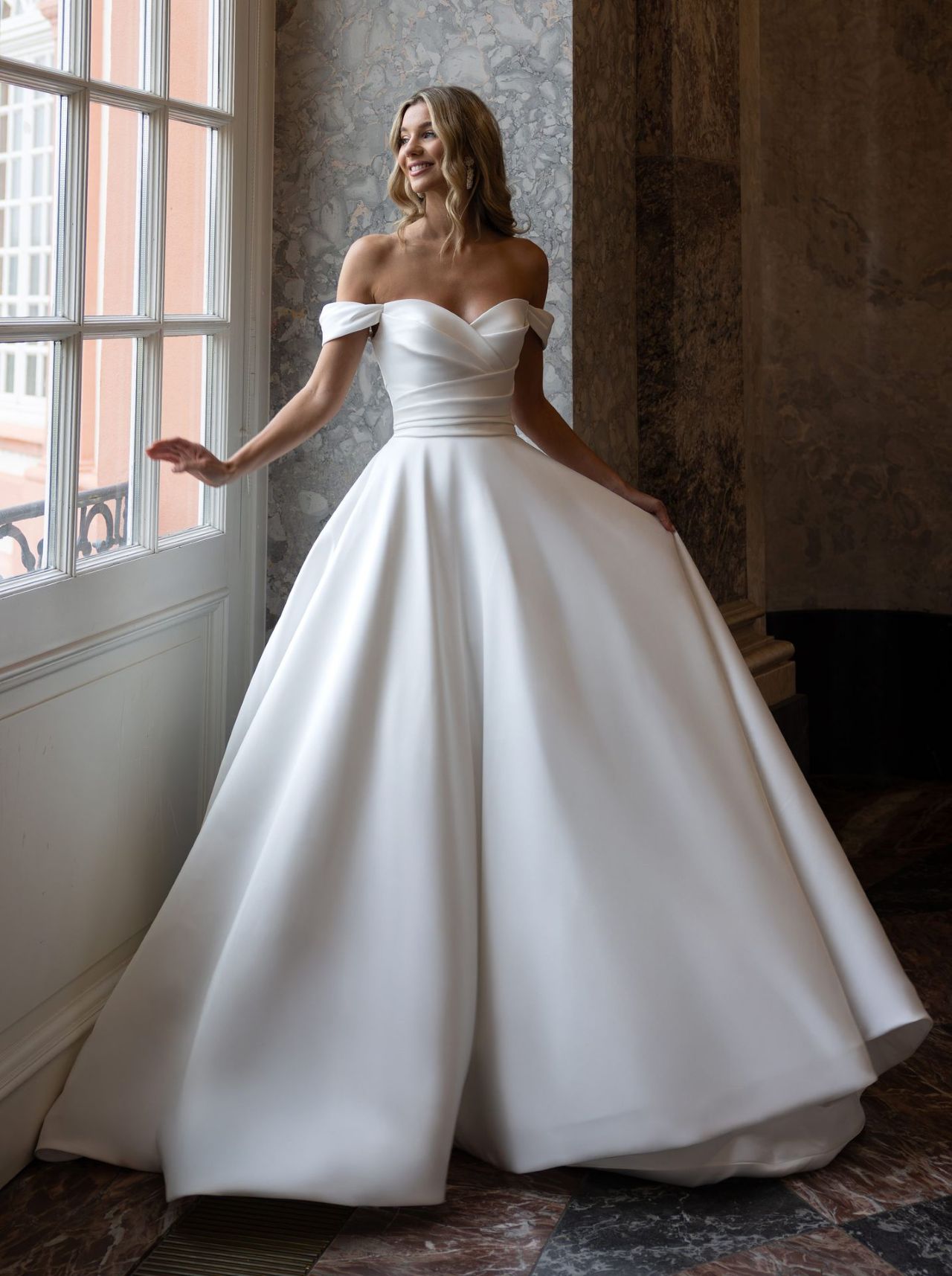 Cleanes Hochzeitskleid mit Off-Shoulder-Ärmeln, herzförmigem Ausschnitt, drapierter Corsage, voluminösem Satinrock, Knopfleiste und langer Schleppe – Vorder- und Rückenansicht bei Brautfashion in