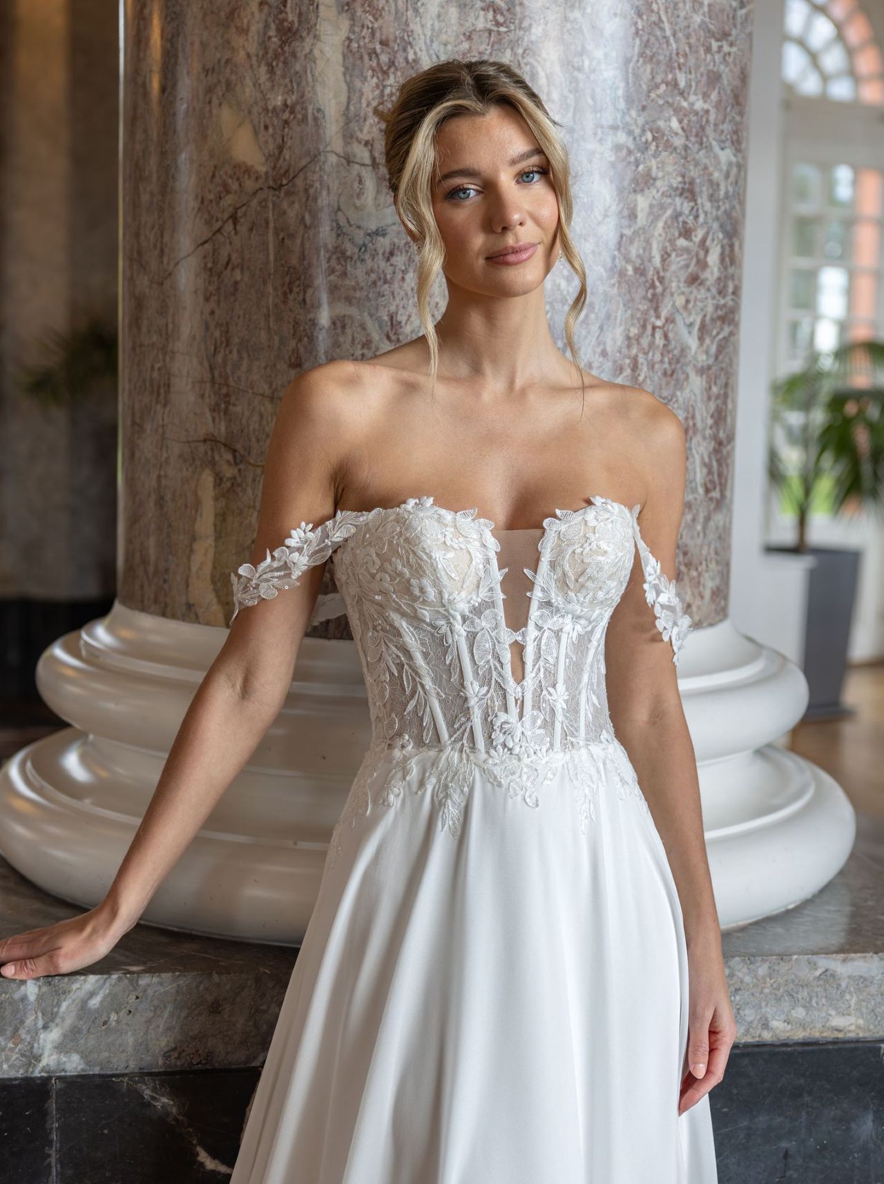 Romantisches Hochzeitskleid mit Off-Shoulder-Spitzenärmeln, transparenter Corsage, tiefem V-Ausschnitt, fliessendem Chiffonrock und langer Schleppe mit Spitzenkante – Vorder- und Rückenansicht bei Brautfashion in Sins