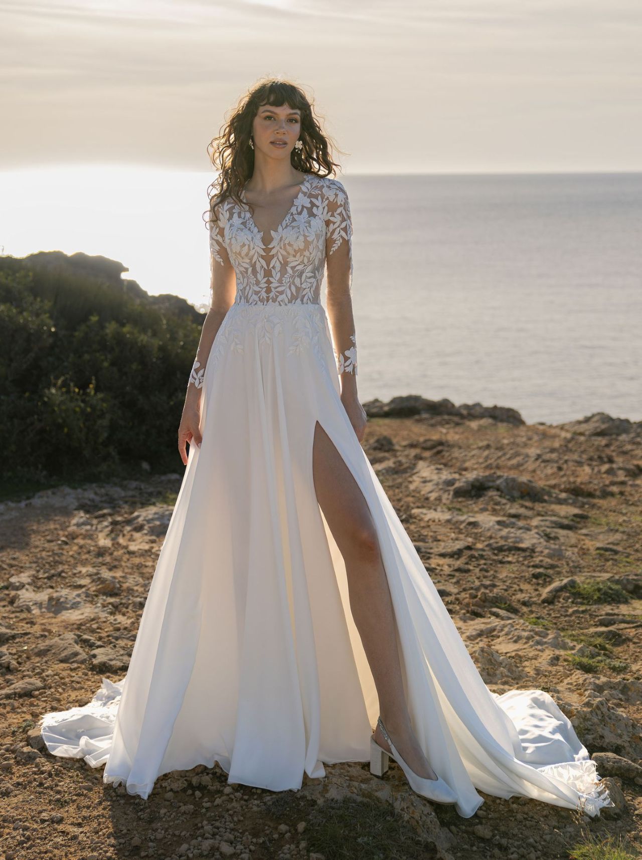 Romantisches Hochzeitskleid mit langen Spitzenärmeln, transparenter Spitzen-Corsage, tiefem V-Ausschnitt, Beinschlitz, fliessendem Rock und langer Schleppe mit floraler Spitzenkante – Vorder- und Rückenansicht bei Brautfashion in Sins