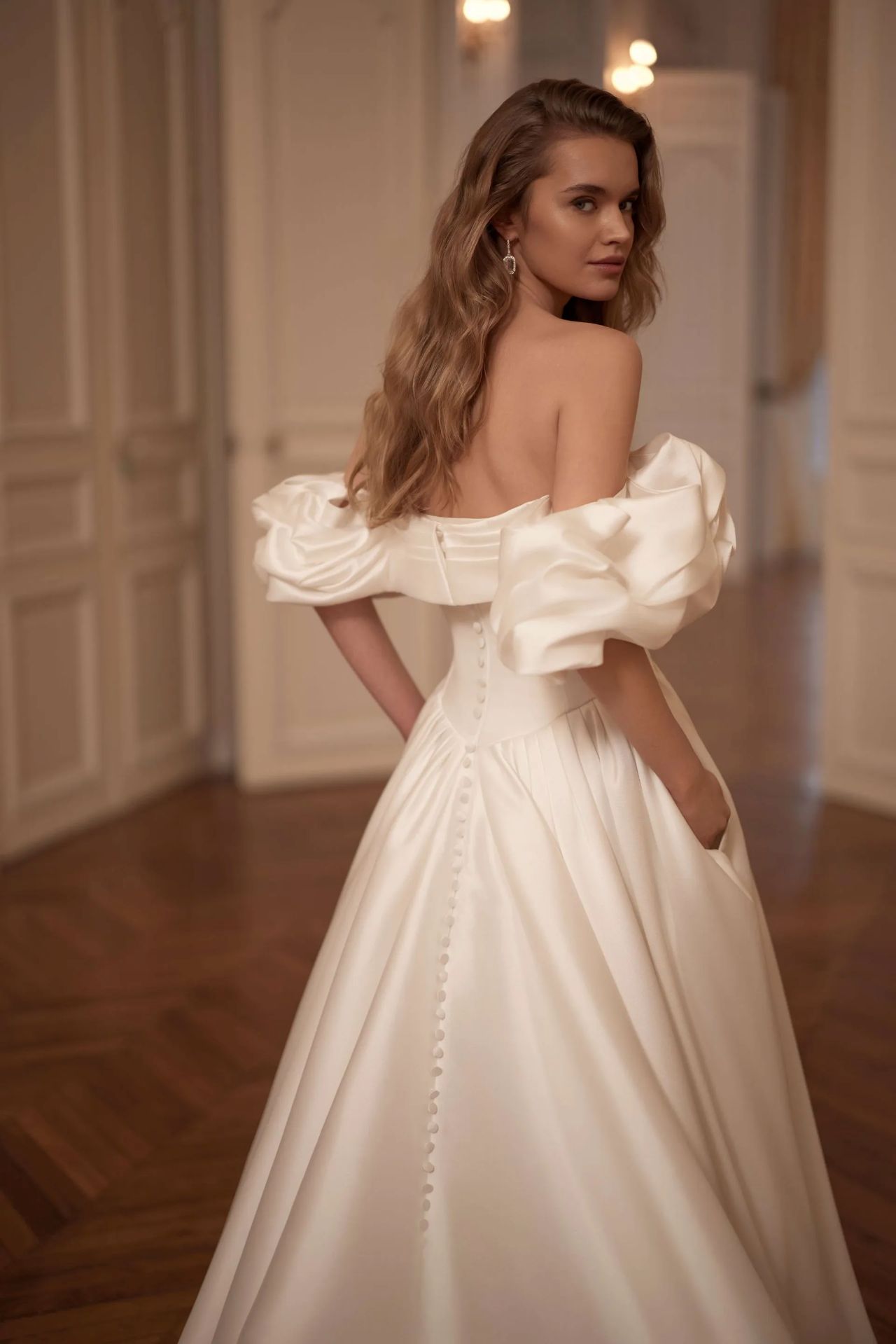 Cleanes Hochzeitskleid mit Off-Shoulder-Statement-Ärmeln, drapierter Corsage, Basque-Taille, voluminösem Rock, Knopfleiste und moderner Prinzessinnen-Silhouette – Vorder- und Rückenansicht bei Brautfashion in Sins