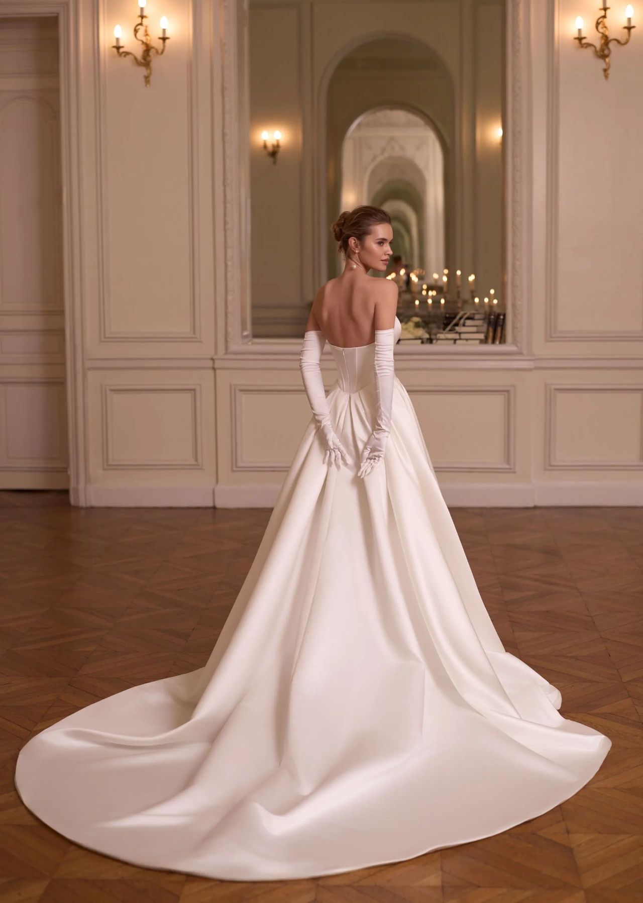 Cleanes Hochzeitskleid mit trägerloser Corsage, asymmetrischem Ausschnitt, Basque-Taille, langen Handschuhen, voluminösem Satinrock, tiefem Rücken, Knopfleiste und langer Schleppe – Vorder- und Rückenansicht bei Brautfashion in Sins